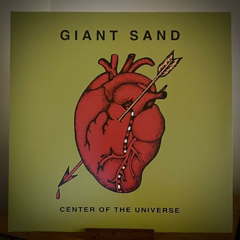 An album cover featuring a bright green background with a prominently illustrated red heart. The heart has an arrow piercing through it and is accompanied by the text "GIANT SAND" at the top and "CENTER OF THE UNIVERSE" at the bottom