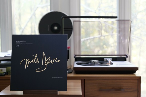 Miles Davis Quintet - The Complete Live in Paris 1960, Vol. I LP cover.

On a dark blue background, Miles' gold signature. In small white type, title, and the label (The Lost Recordings). Handwritten, it's number 1331.

The black LP plays on a vintage, restored Bang & Olufsen Beogram 4000 linear-tracking turntable to the right.