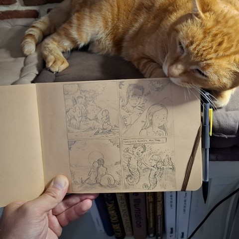 A photo of my hand holding an A5 landscape sketchbook with tobacco-colored paper. The story on it is a sketch of "The centaur and the siren" (previous post on my timeline for the details of this story). A disposable plastic mechanical pencil with an eraser is attached to the notebook. My ginger cat in background is chewing on the elastic band.