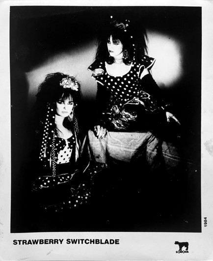 black and white shot from across the room. High contrast so subtle details are lost. Both wear a lot of white polka dots.